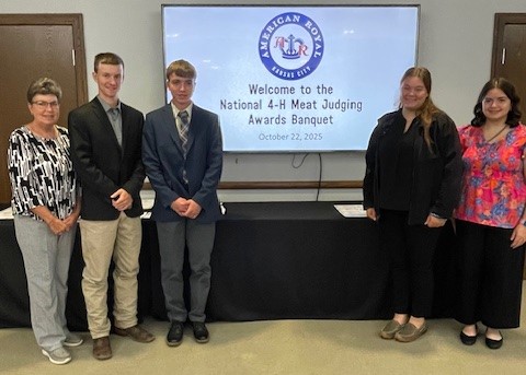 Four youth and one adult standing in front of a sign that says "Welcome to the National 4-H Meats Judging Contest Awards Banquet."
